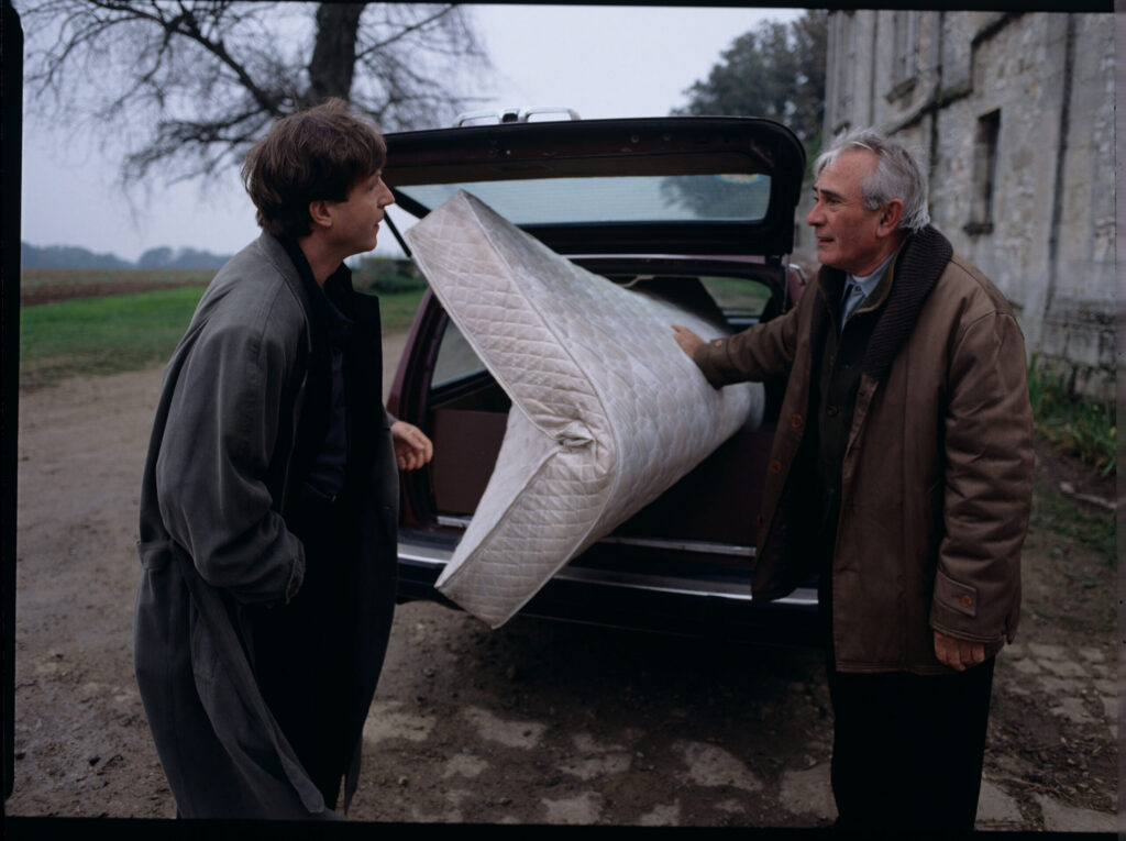 Oliviere (Régent) carries the mattress to the car with the help of a gardener (Forget). The scene was not shown in the film.