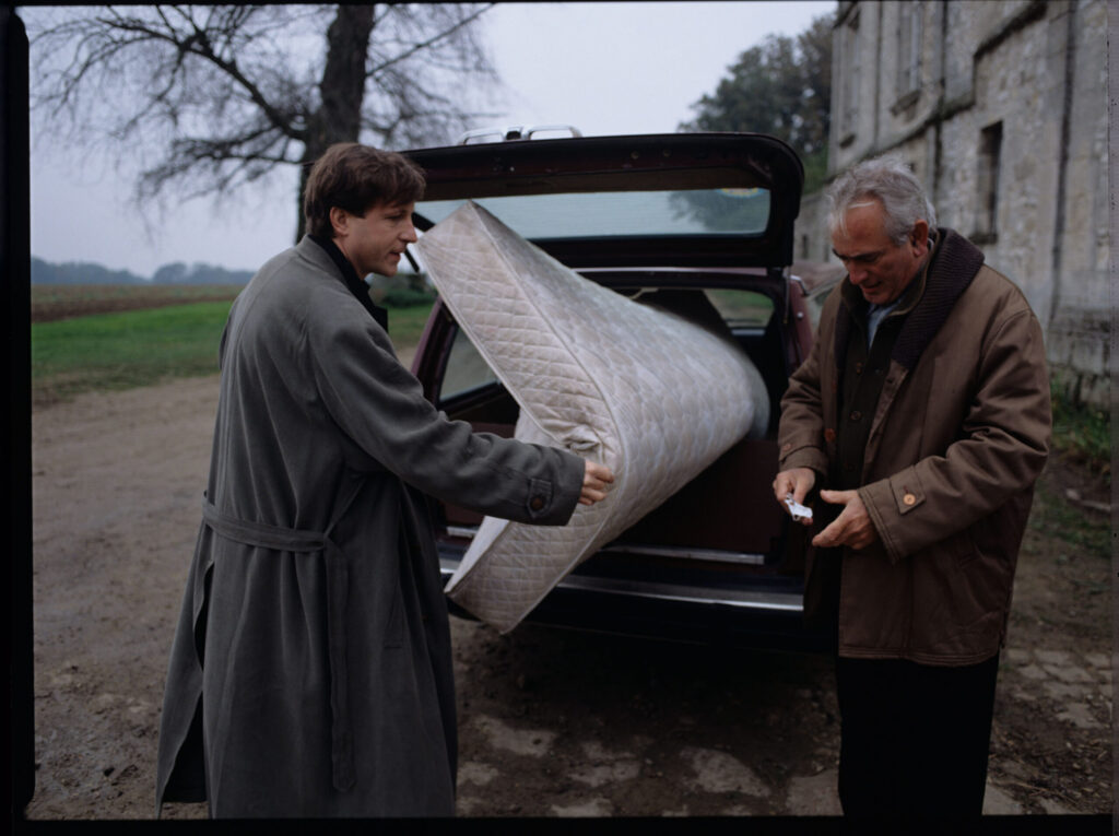 Oliviere (Régent) carries the mattress to the car with the help of a gardener (Forget). The scene was not shown in the film.