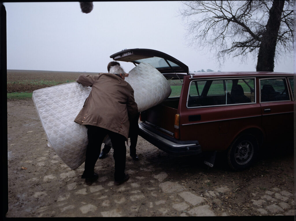 Oliviere (Régent) carries the mattress to the car with the help of a gardener (Forget). The scene was not shown in the film.