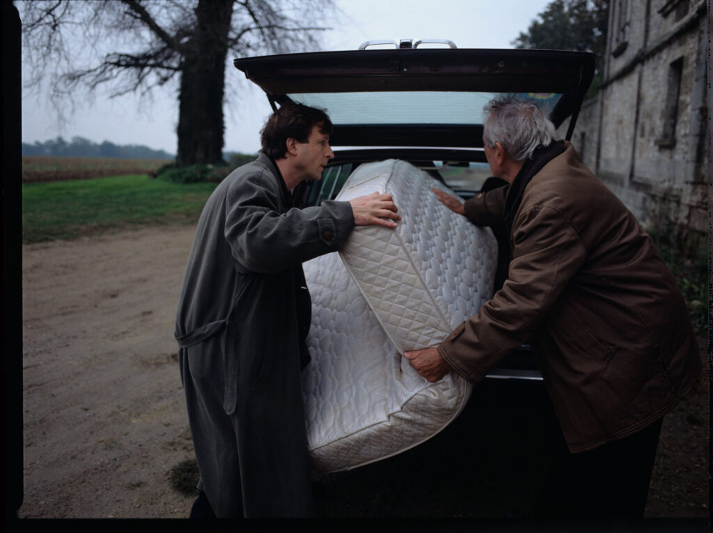 Oliviere (Régent) carries the mattress to the car with the help of a gardener (Forget). The scene was not shown in the film.
