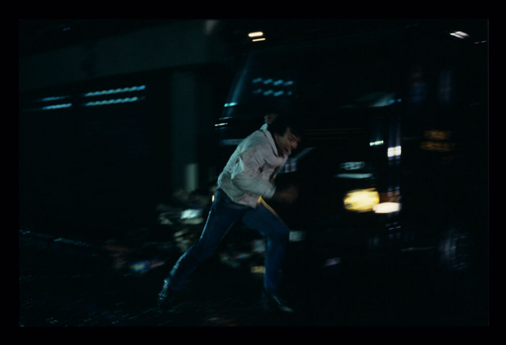 A man running away from attackers on the street under the windows of the main character of the film.