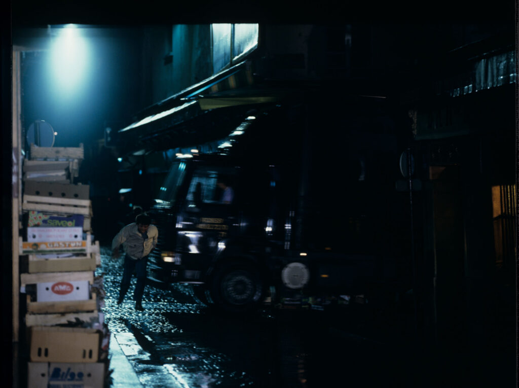 A man running away from attackers on the street under the windows of the main character of the film.