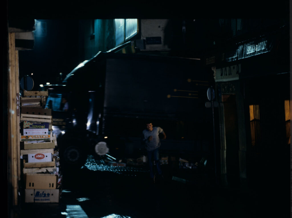 A man running away from attackers on the street under the windows of the main character of the film.