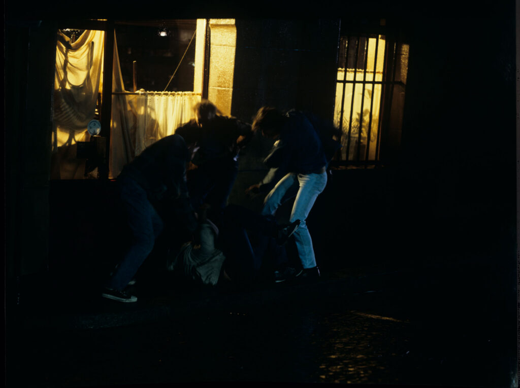A scene of a street fight which the terrified Julie observes through the window of her apartment.