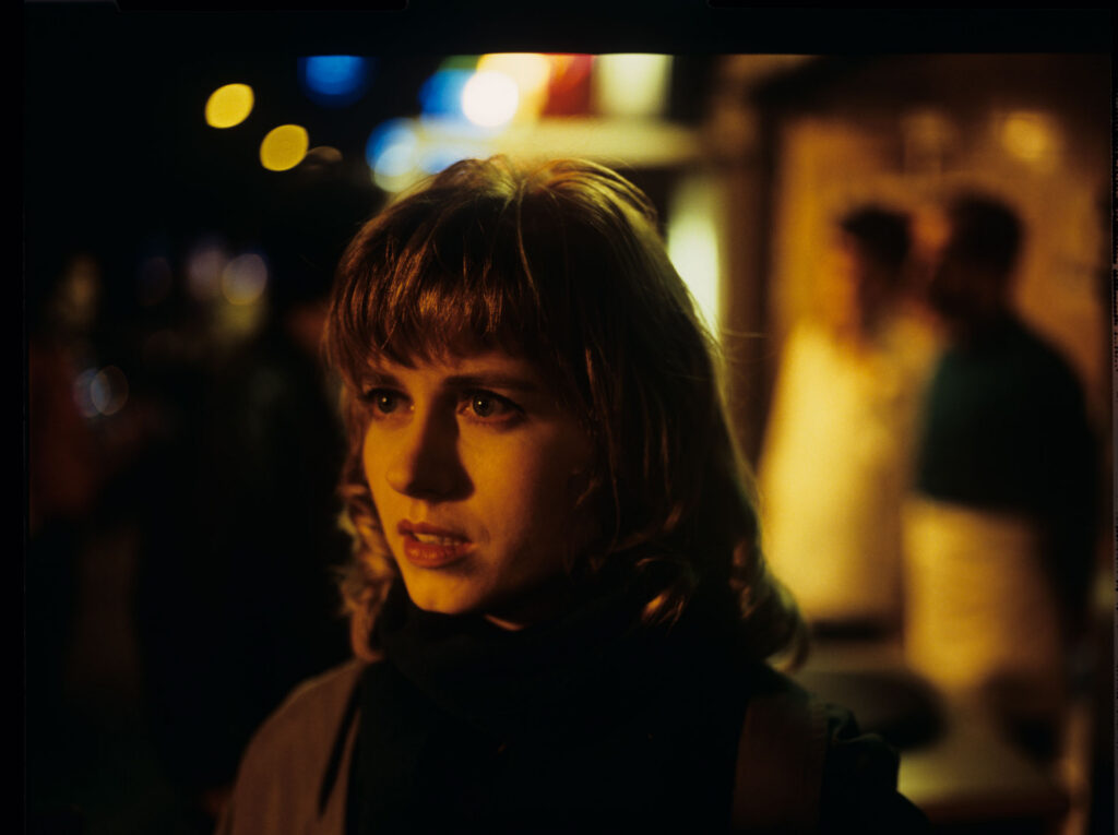 Lucille (Charlotte Very), Julie's neighbor who works at a nightclub, on a Parisian street.