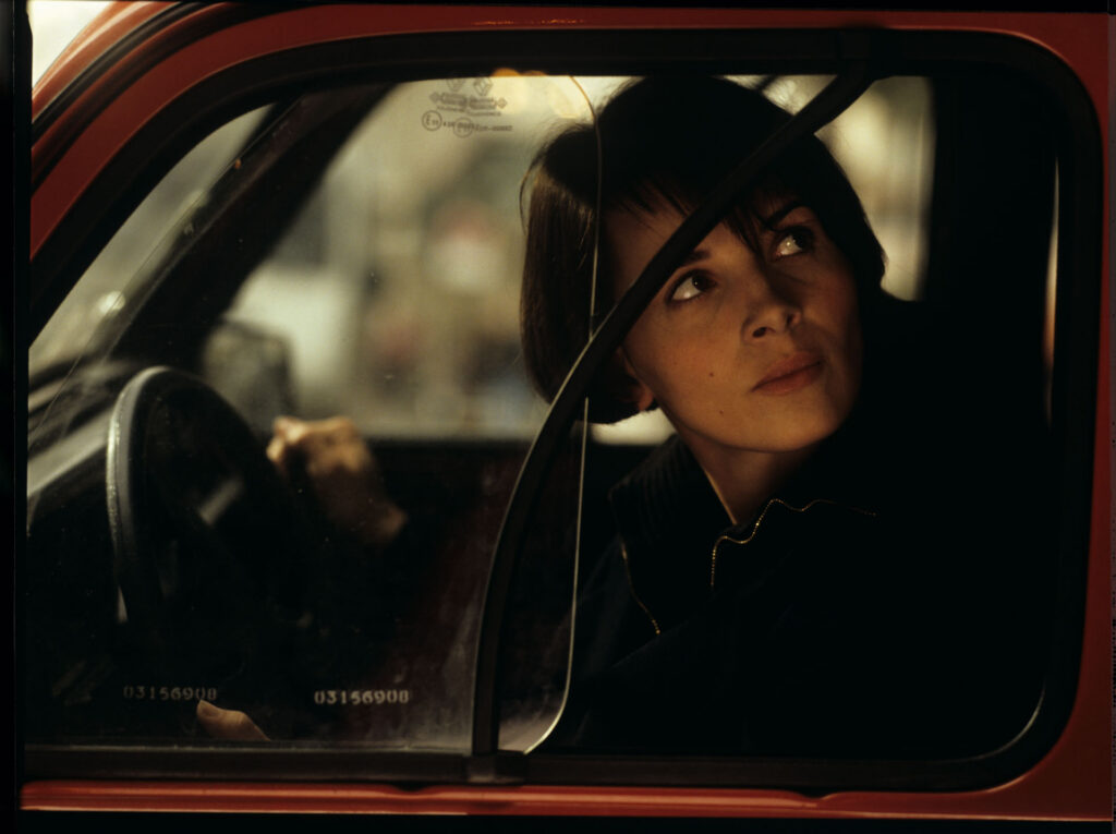 Julie (Juliette Binoche) is talking to a journalist (Helene Vincent) through her car window.