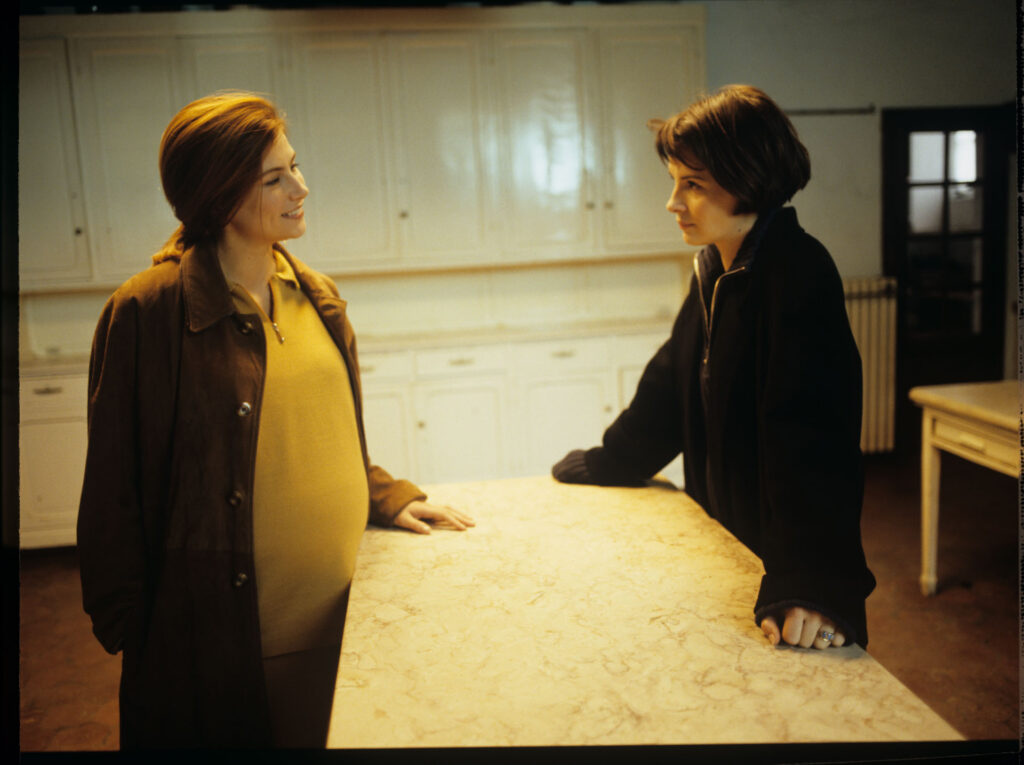 Sandrine (Florence Pernel) and Julie (Juliette Binoche) are talking in the kitchen of Julie and Patrice's suburban house
