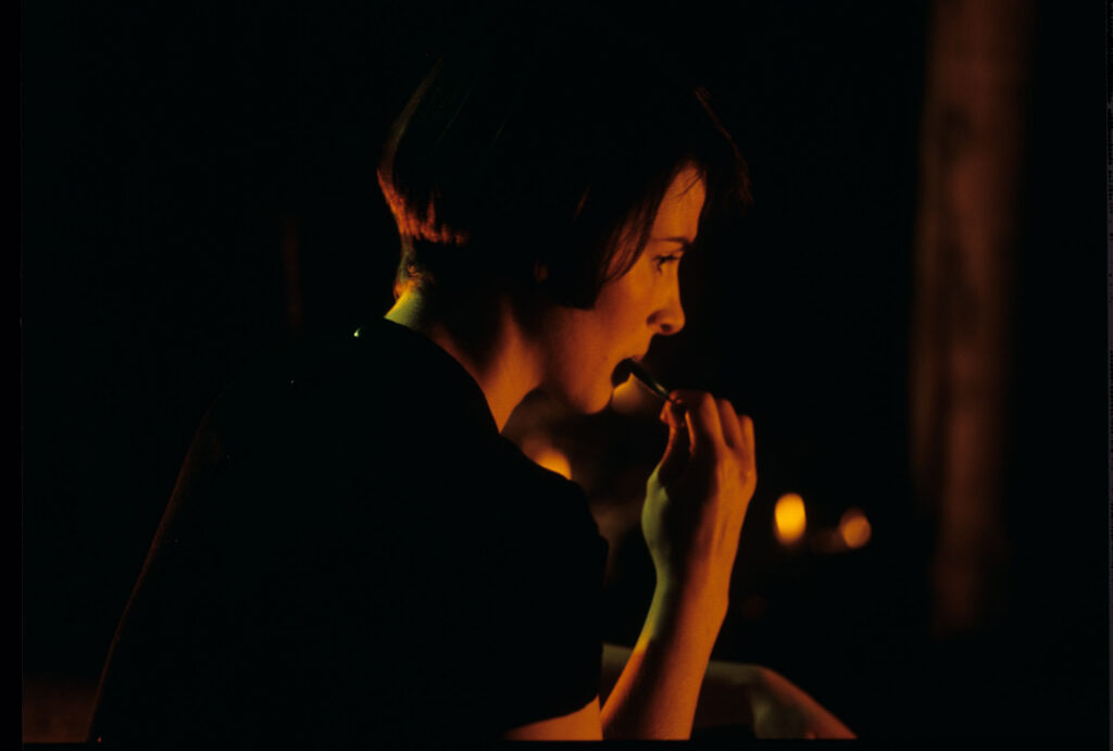Julie (Juliette Binoche) takes a blue lollipop from her purse in front of the fireplace in an emptied room.