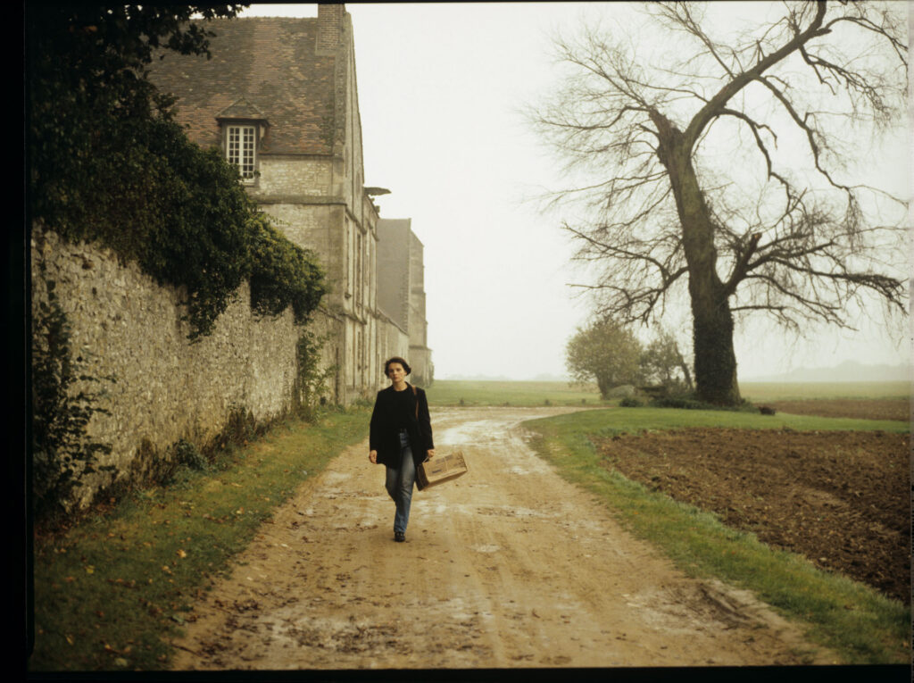 Julie (Juliette Binoche) walking along a stone wall that surrounds the suburban house of her tragically deceased husband.
