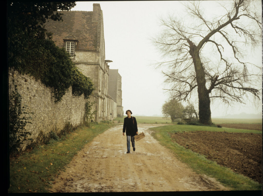 Julie (Juliette Binoche) walking along a stone wall that surrounds the suburban house of her tragically deceased husband.