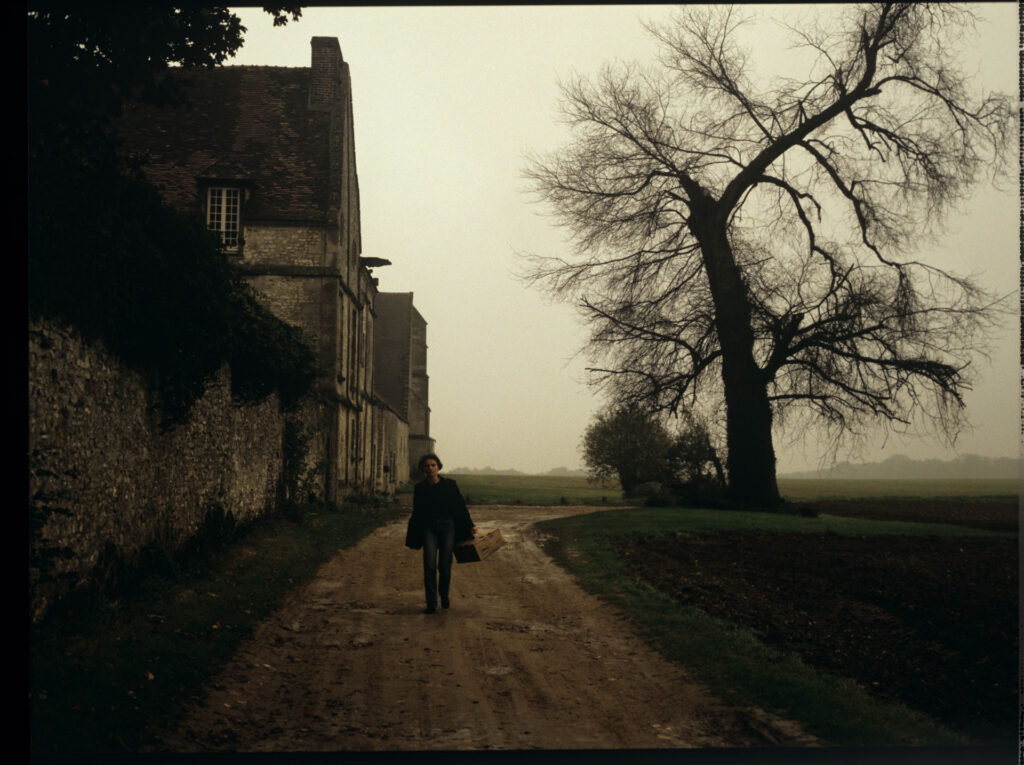 Julie (Juliette Binoche) walking along a stone wall that surrounds the suburban house of her tragically deceased husband.