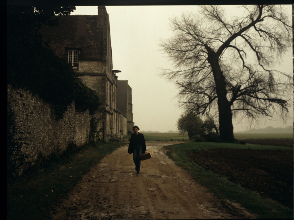 Julie (Juliette Binoche) walking along a stone wall that surrounds the suburban house of her tragically deceased husband.