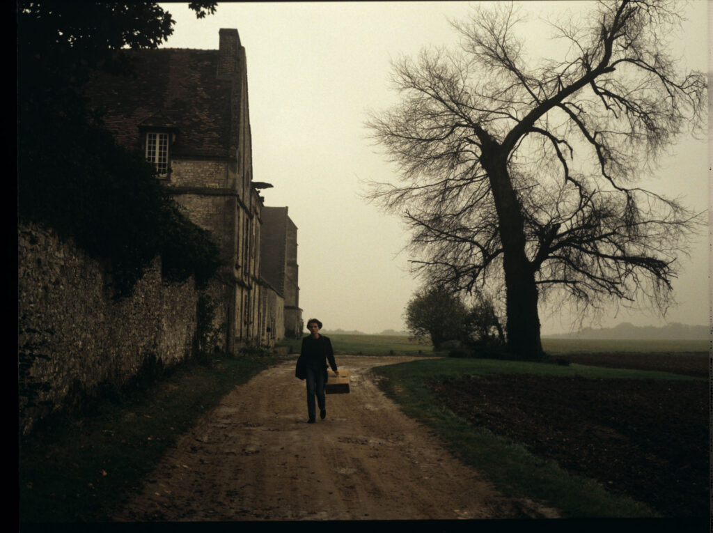 Julie (Juliette Binoche) walking along a stone wall that surrounds the suburban house of her tragically deceased husband.