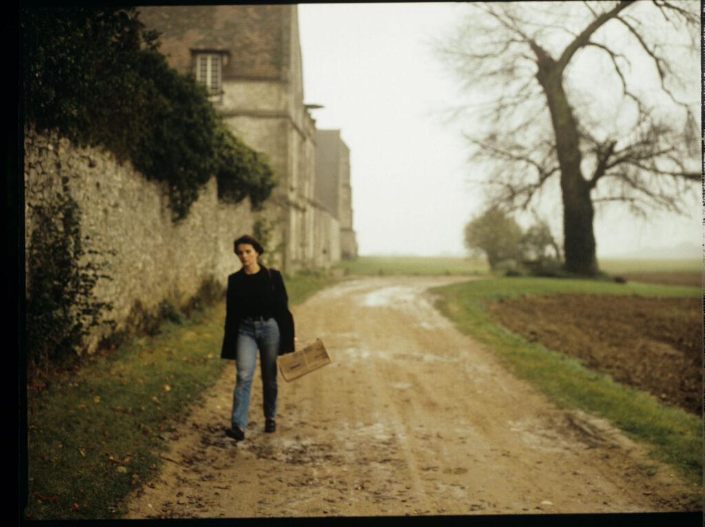 Julie (Juliette Binoche) walking along a stone wall that surrounds the suburban house of her tragically deceased husband.