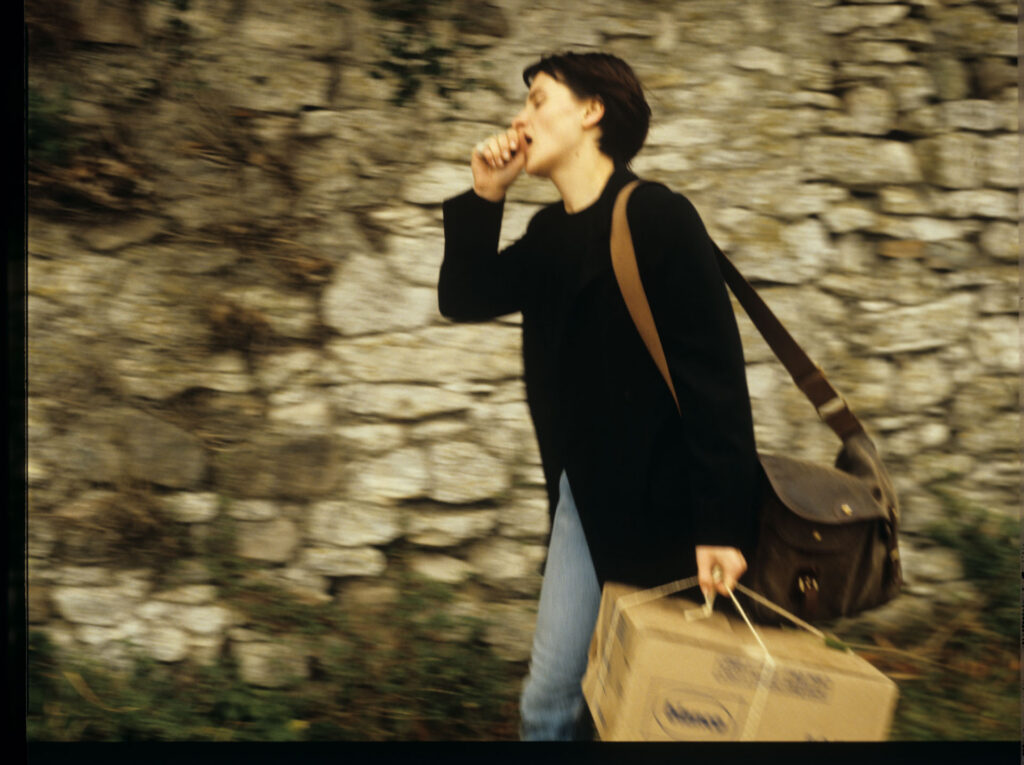 Julie (Juliette Binoche) walking along a stone wall that surrounds the suburban house of her tragically deceased husband.
