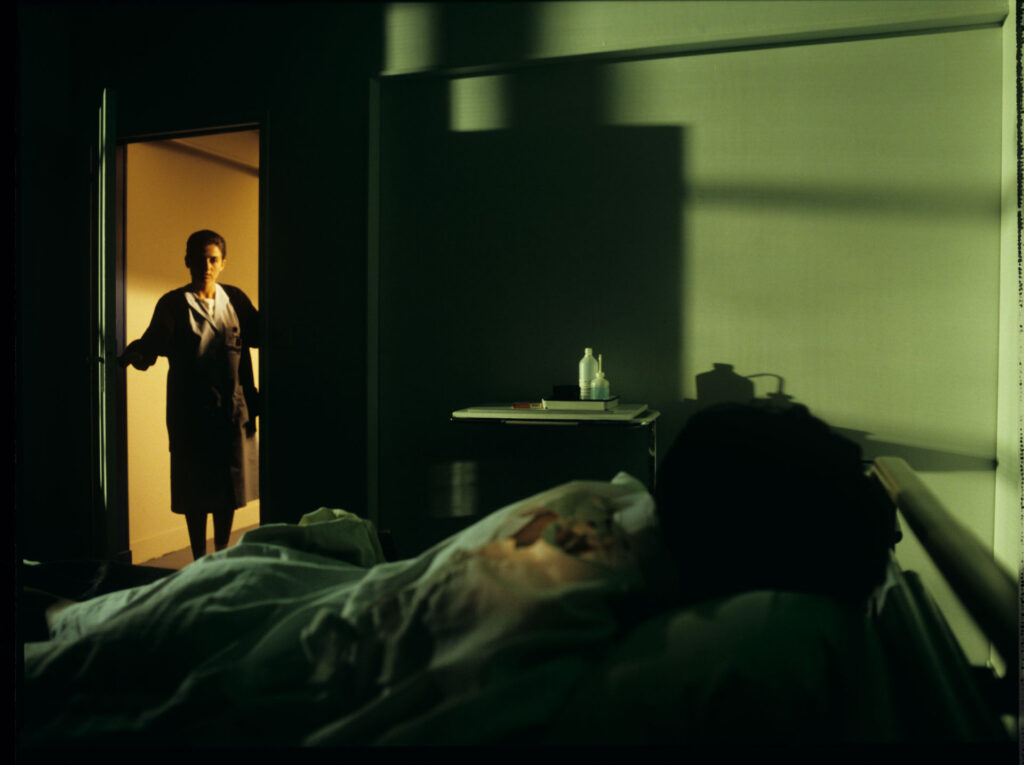 A nurse (Idit Cebula) peeks into the hospital room where Julie (Juliette Binoche) is lying.