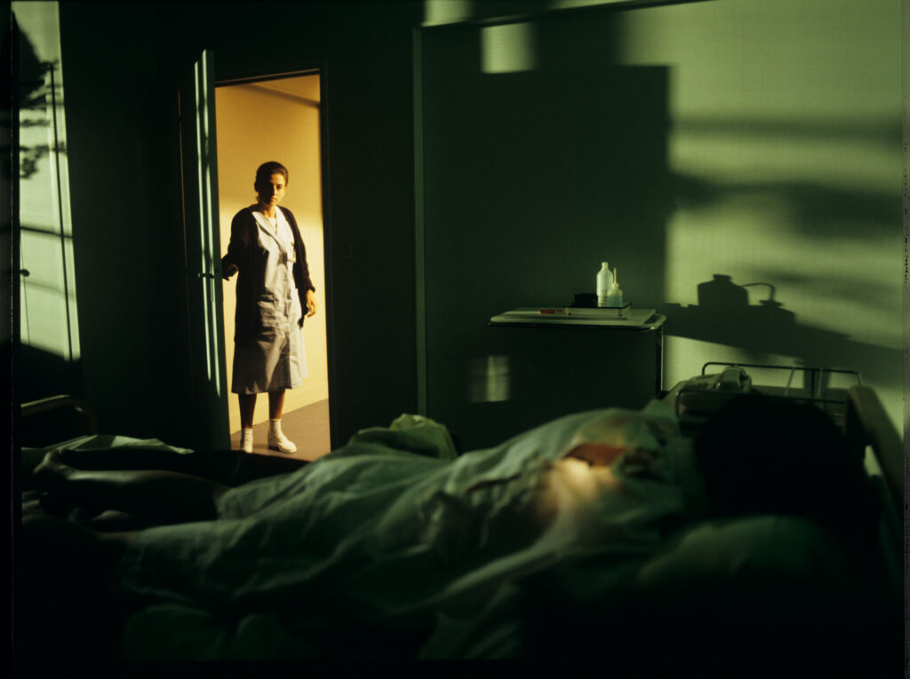 A nurse (Idit Cebula) peeks into the hospital room where Julie (Juliette Binoche) is lying.