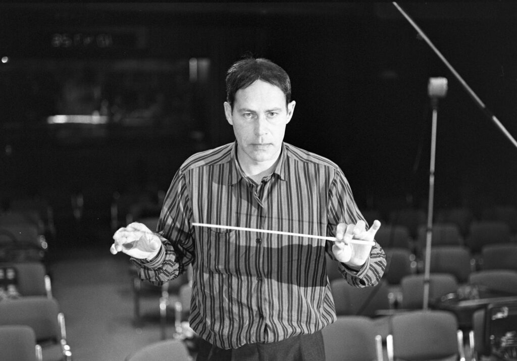 A photograph of the composer Patrice de Courcy (Hugues Quester) rehearsing with the orchestra.