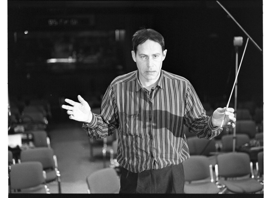 A photograph of the composer Patrice de Courcy (Hugues Quester) rehearsing with the orchestra.
