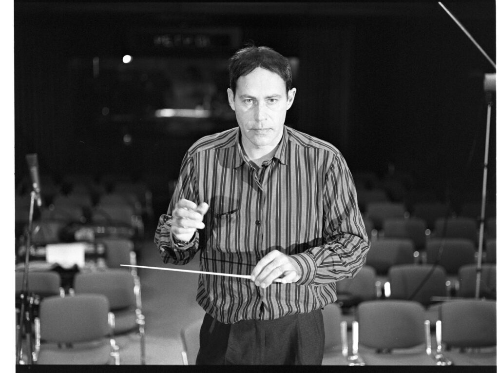 A photograph of the composer Patrice de Courcy (Hugues Quester) rehearsing with the orchestra.