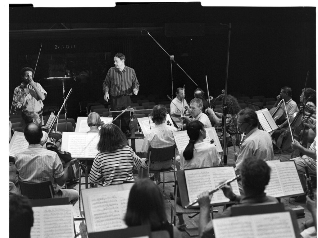 A photograph of the composer Patrice de Courcy (Hugues Quester) rehearsing with the orchestra.