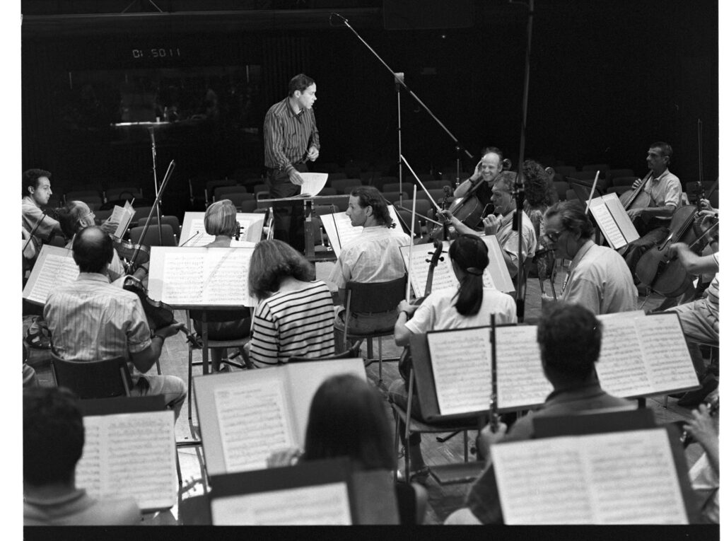 A photograph of the composer Patrice de Courcy (Hugues Quester) rehearsing with the orchestra.