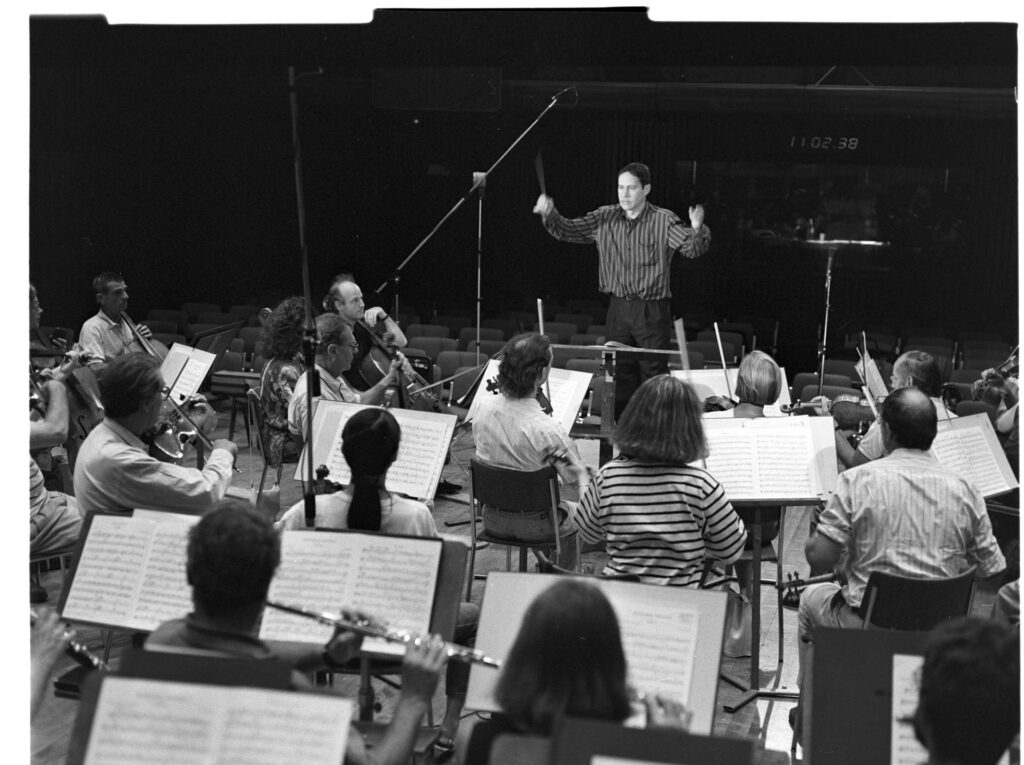 A photograph of the composer Patrice de Courcy (Hugues Quester) rehearsing with the orchestra.