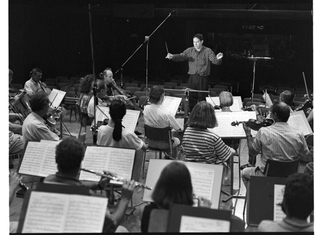 A photograph of the composer Patrice de Courcy (Hugues Quester) rehearsing with the orchestra.
