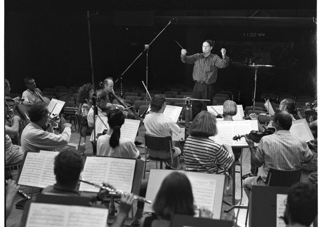 A photograph of the composer Patrice de Courcy (Hugues Quester) rehearsing with the orchestra.