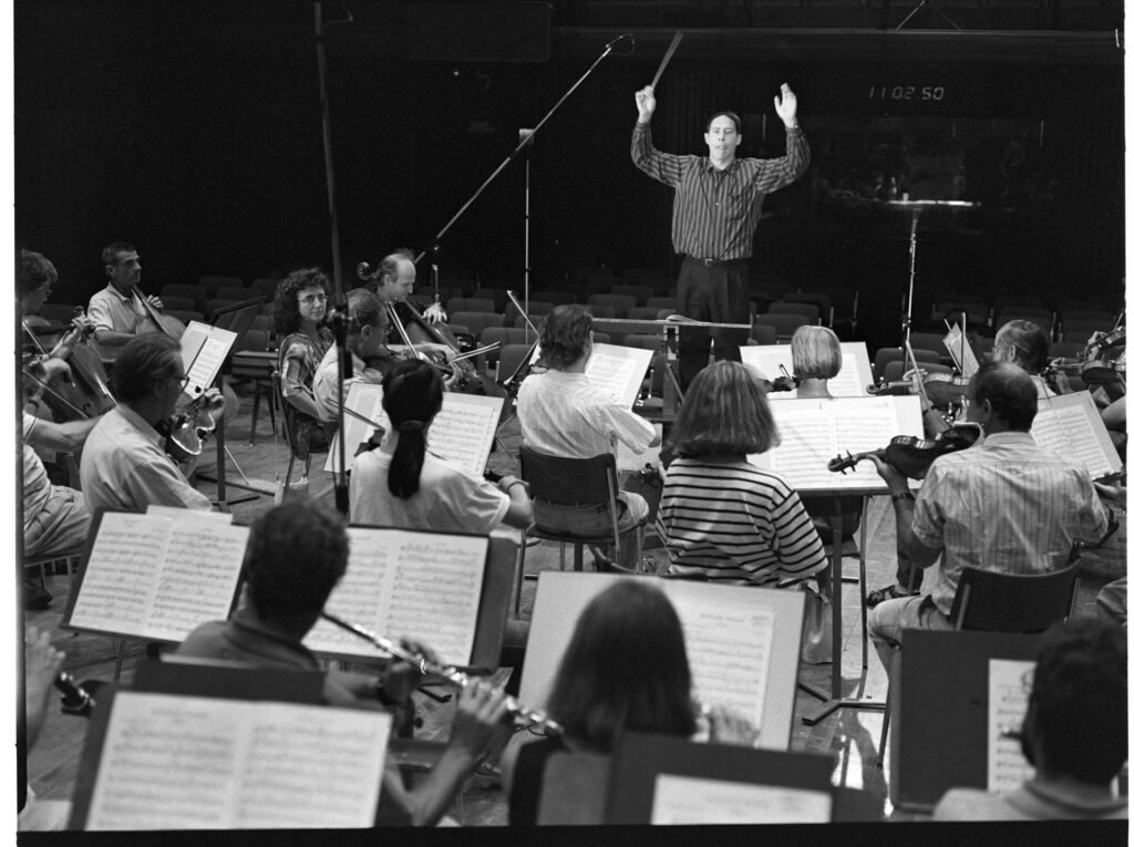 A photograph of the composer Patrice de Courcy (Hugues Quester) rehearsing with the orchestra.