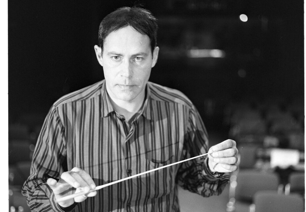 A photograph of the composer Patrice de Courcy (Hugues Quester) rehearsing with the orchestra.