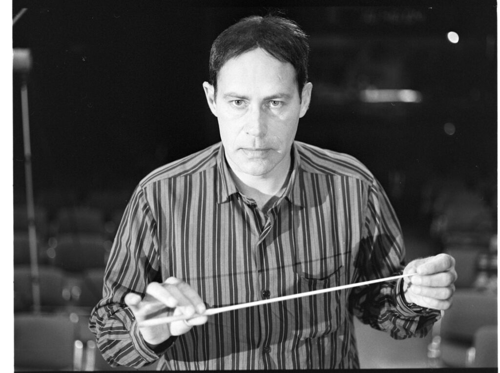 A photograph of the composer Patrice de Courcy (Hugues Quester) rehearsing with the orchestra.