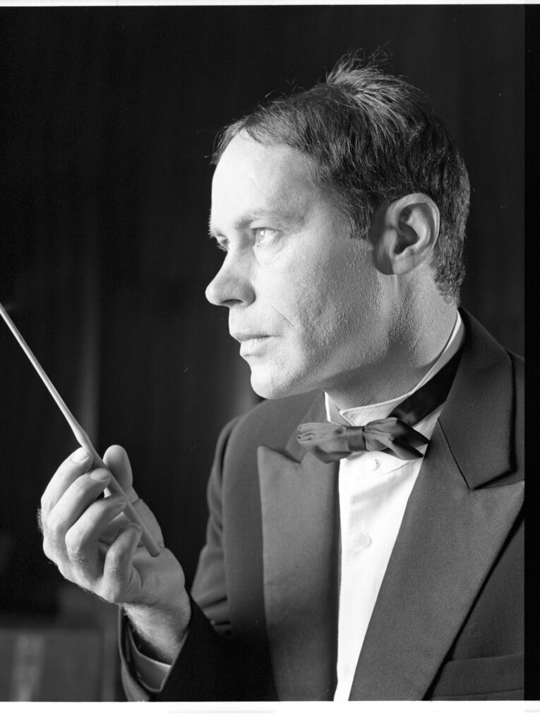 A photograph of the composer Patrice de Courcy (Hugues Quester) rehearsing with the orchestra.