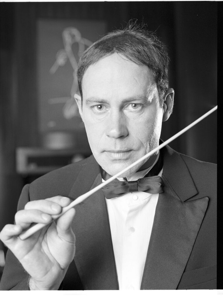 A photograph of the composer Patrice de Courcy (Hugues Quester) rehearsing with the orchestra.