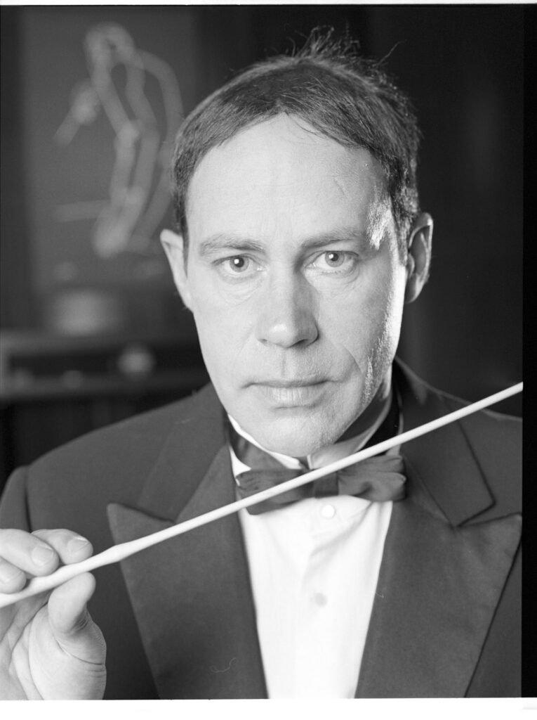 A photograph of the composer Patrice de Courcy (Hugues Quester) rehearsing with the orchestra.