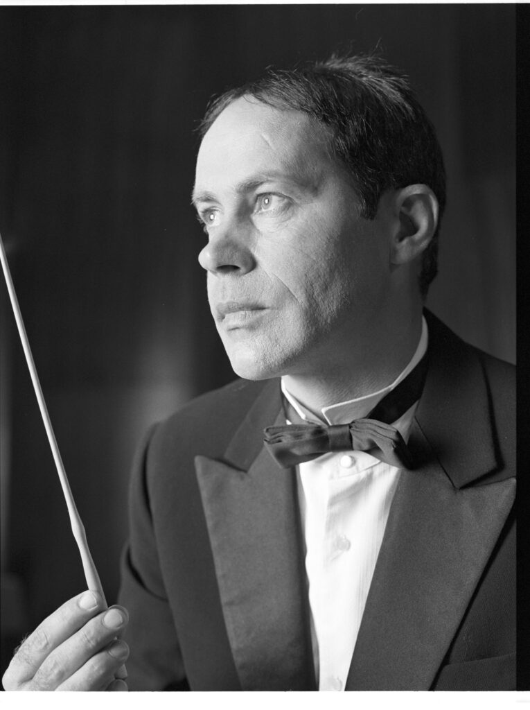 A photograph of the composer Patrice de Courcy (Hugues Quester) rehearsing with the orchestra.