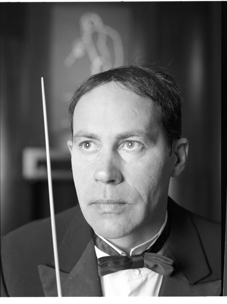 A photograph of the composer Patrice de Courcy (Hugues Quester) rehearsing with the orchestra.