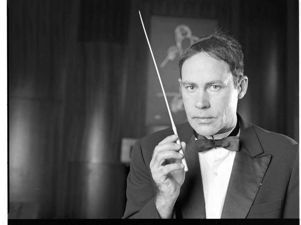A photograph of the composer Patrice de Courcy (Hugues Quester) rehearsing with the orchestra.