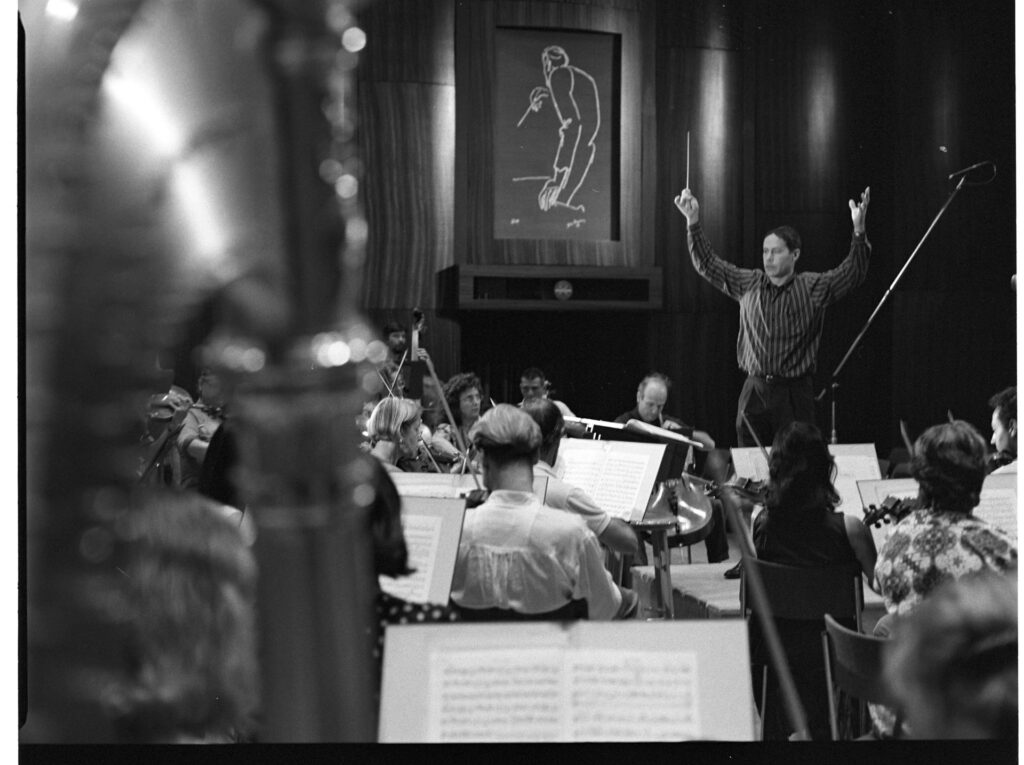 A photograph of the composer Patrice de Courcy (Hugues Quester) rehearsing with the orchestra.