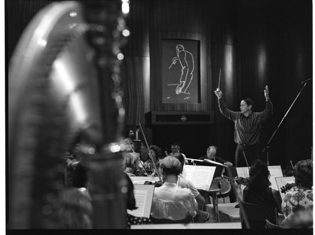 A photograph of the composer Patrice de Courcy (Hugues Quester) rehearsing with the orchestra.