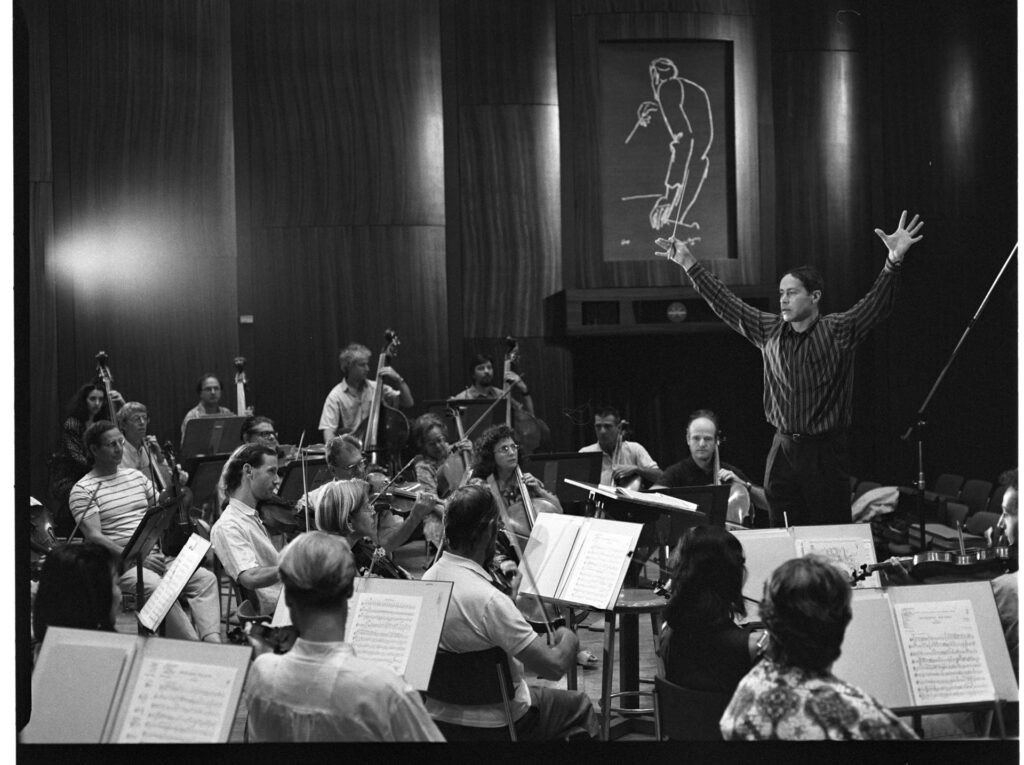 A photograph of the composer Patrice de Courcy (Hugues Quester) rehearsing with the orchestra.