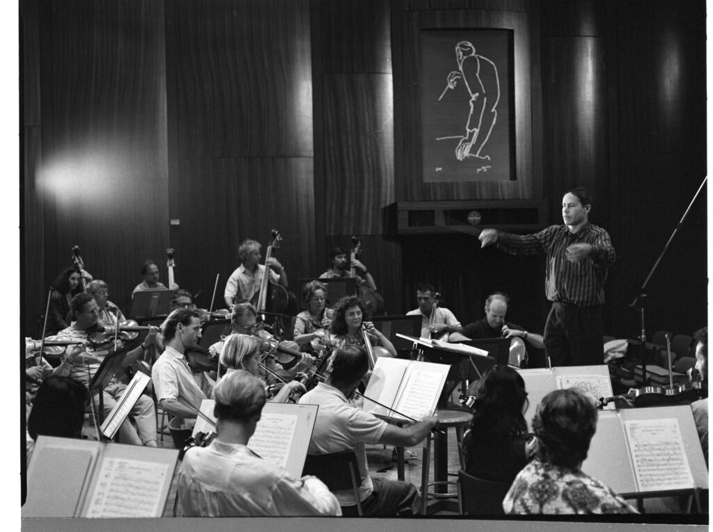 A photograph of the composer Patrice de Courcy (Hugues Quester) rehearsing with the orchestra.