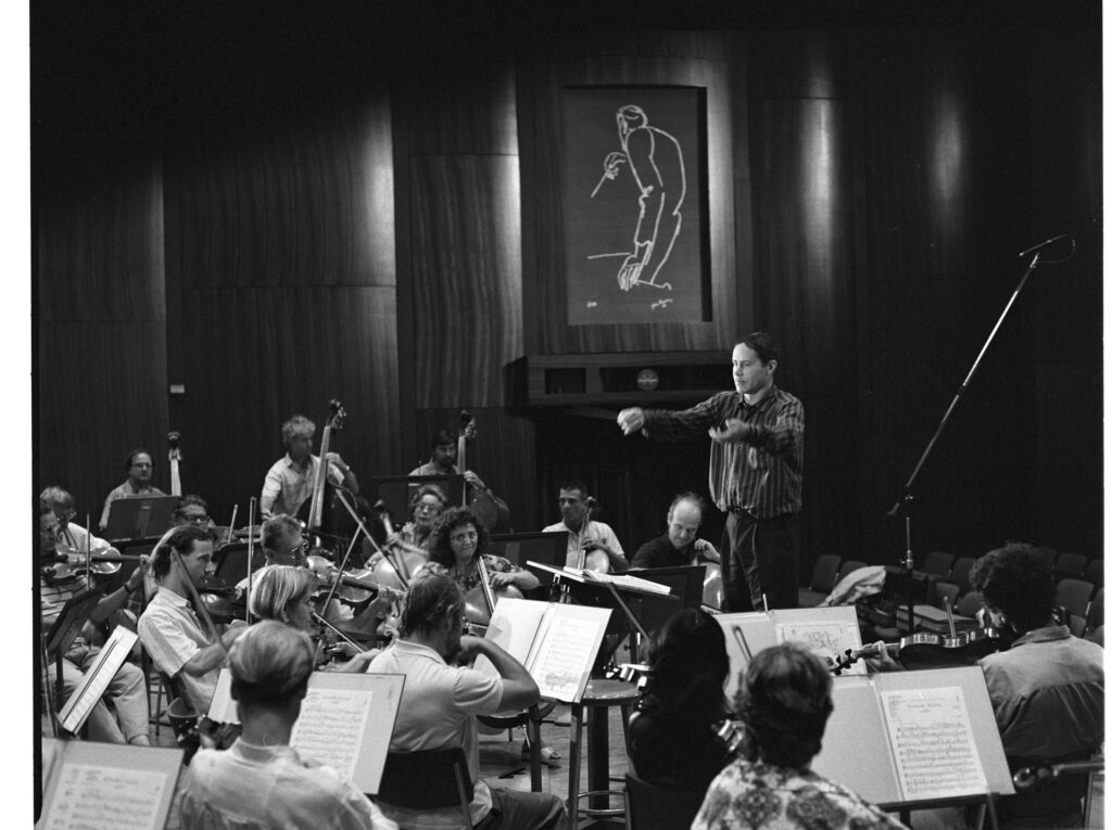 A photograph of the composer Patrice de Courcy (Hugues Quester) rehearsing with the orchestra.