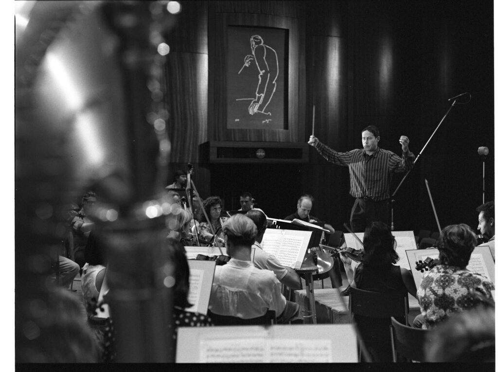 A photograph of the composer Patrice de Courcy (Hugues Quester) rehearsing with the orchestra.