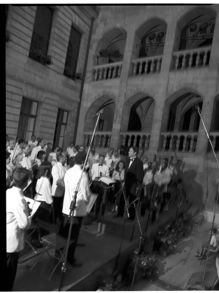 A photograph of the composer Patrice de Courcy (Hugues Quester) rehearsing with the orchestra.
