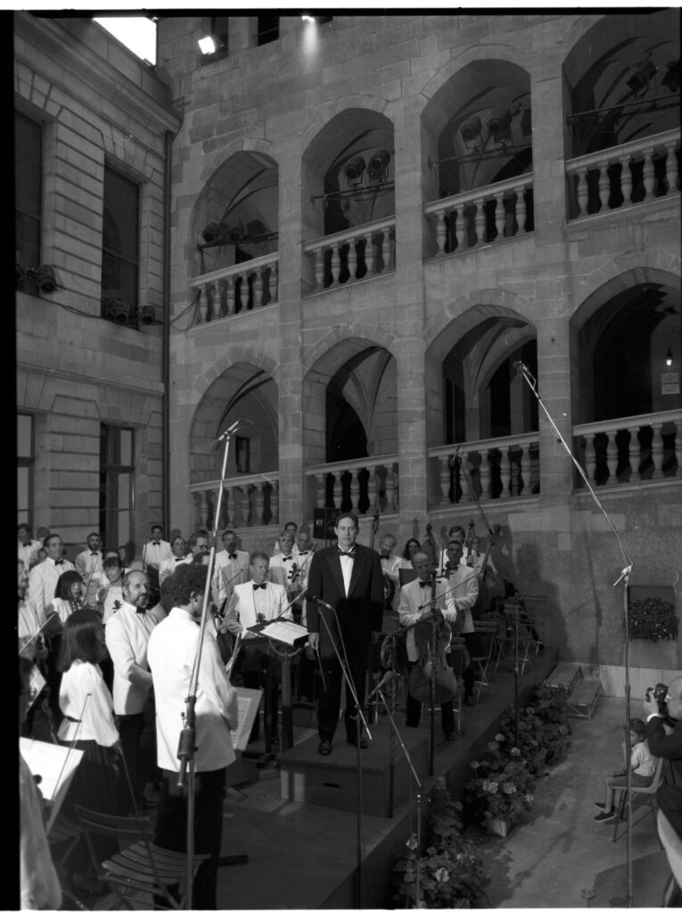 A photograph of the composer Patrice de Courcy (Hugues Quester) rehearsing with the orchestra.