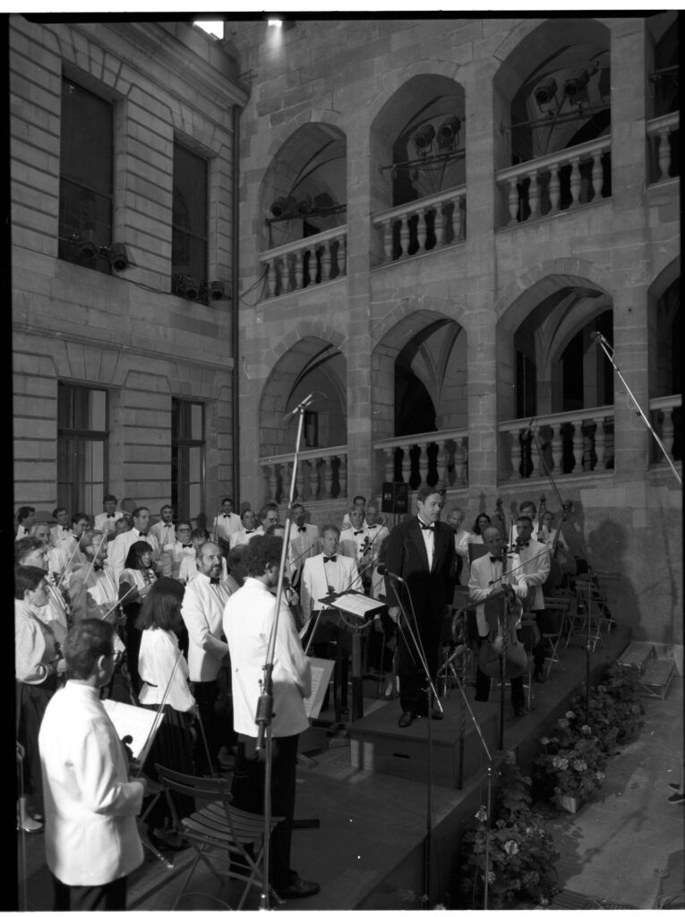A photograph of the composer Patrice de Courcy (Hugues Quester) rehearsing with the orchestra.