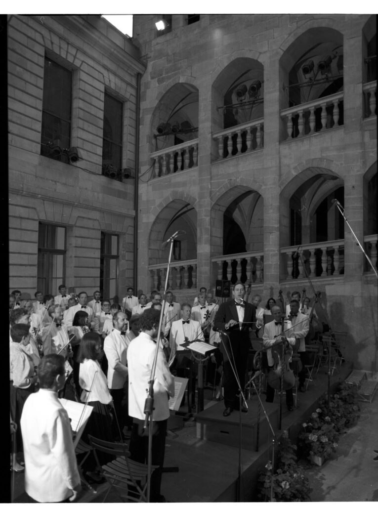 A photograph of the composer Patrice de Courcy (Hugues Quester) rehearsing with the orchestra.