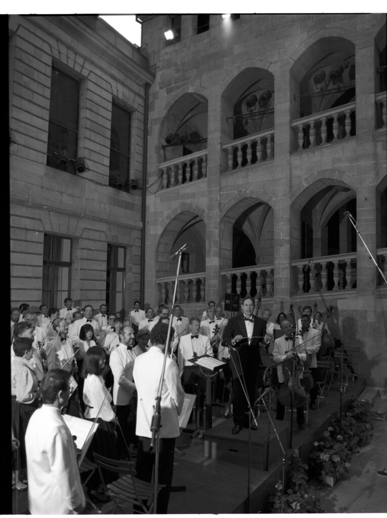 A photograph of the composer Patrice de Courcy (Hugues Quester) rehearsing with the orchestra.