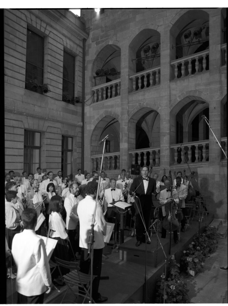 A photograph of the composer Patrice de Courcy (Hugues Quester) rehearsing with the orchestra.